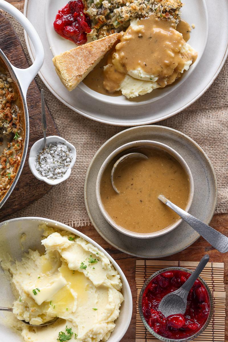 a bowl of dairy free gravy beside mashed potatoes, cranberry sauce, and a vegetarian thanksgiving dinner
