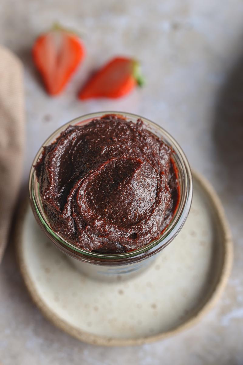 a jar of homemade vegan nutella plus a handful of strawberries dipped in the chocolate spread