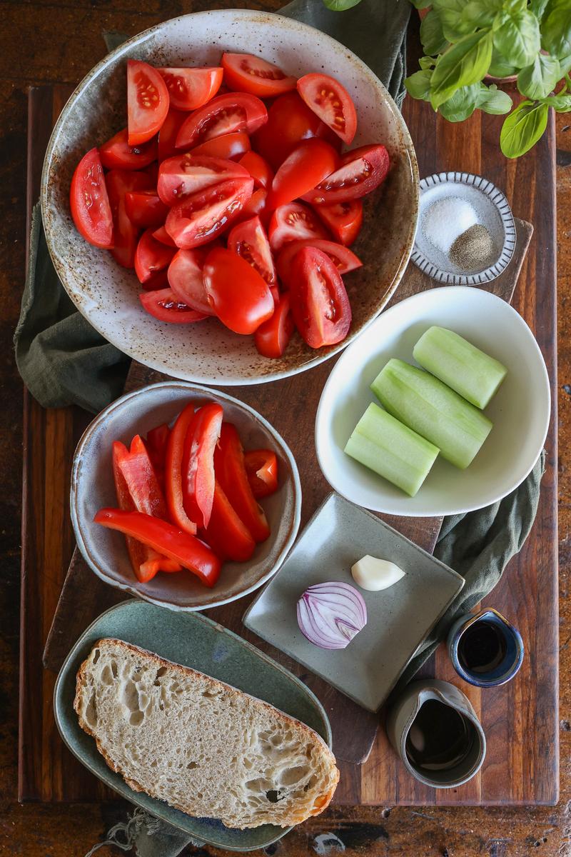 a bowl of tomatoes, zucchini, bell pepper, onion, sauces, and a side of bread