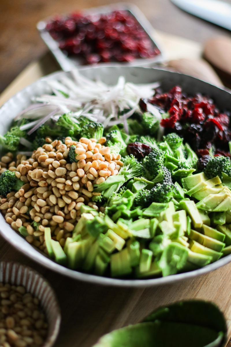 a bowl of broccoli pieces, cranberries, pine nuts, shallot, and avocado cubes