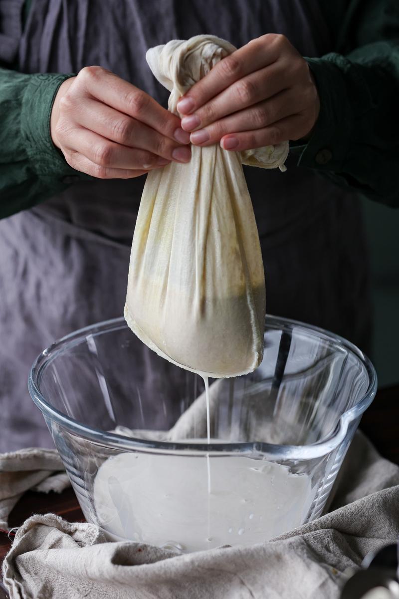 A vegan straining barista oat-based alternative through a cheesecloth.